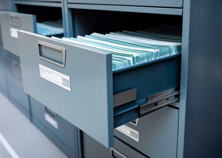 Ein Aktenschrank, dessen Schubladen geöffnet sind und in denen Register zu sehen sind.