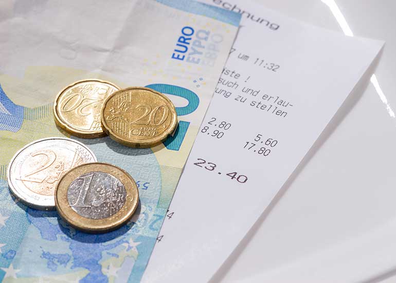 Auf einem Tisch liegen ein Rechnungsbeleg sowie Euro-Banknoten und -Münzen.