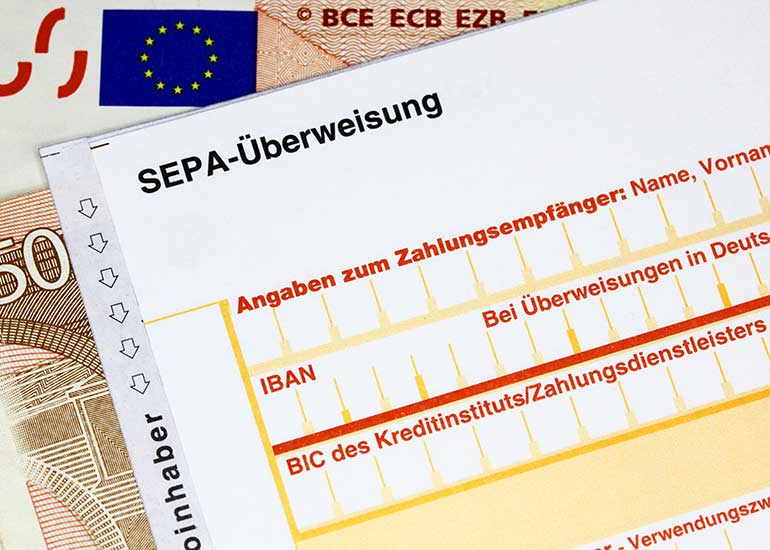 Detailansicht auf eine SEPA-Überweisungsformular darunter liegen Euro-Banknoten.