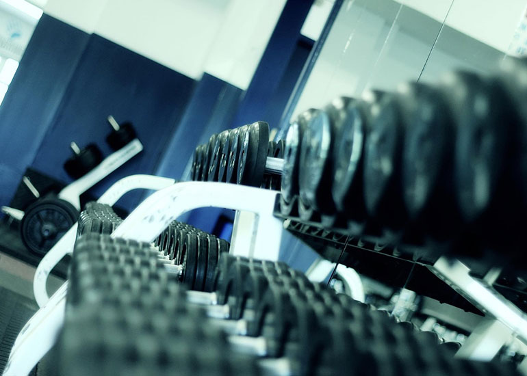 Blick in ein Fitnessstudio. In den Regalen sind viele nach Größe sortierte Gewichte für Hanteln zu sehen.