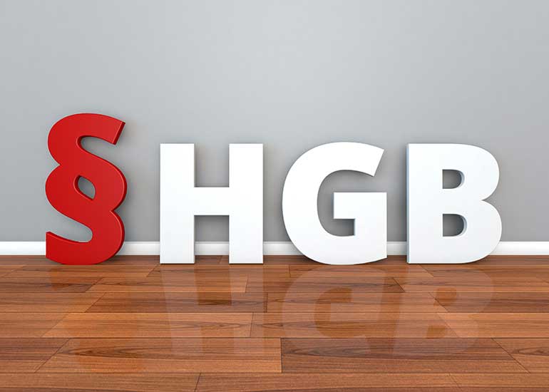 Die Buchstaben „§HGB” stehen auf einem Pakettboden vor einer Wand.