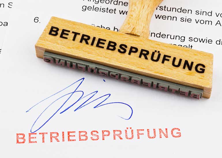 Auf einem Blatt Papier, auf dem der Ausdruck „Betriebsprüfung” abgedruckt ist, liegt ein Stempel mit derselben Aufschrift.