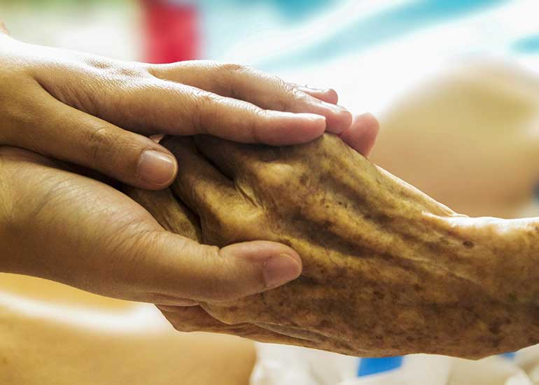 Eine jüngere Person hält die Hand einer älteren Person.