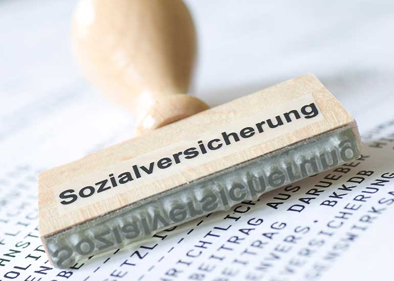 Zu sehen ist ein Stempel mit der Aufschrift „Sozialversicherung”. Er liegt auf einem Blatt Papier, das mit Text bedruckt ist.