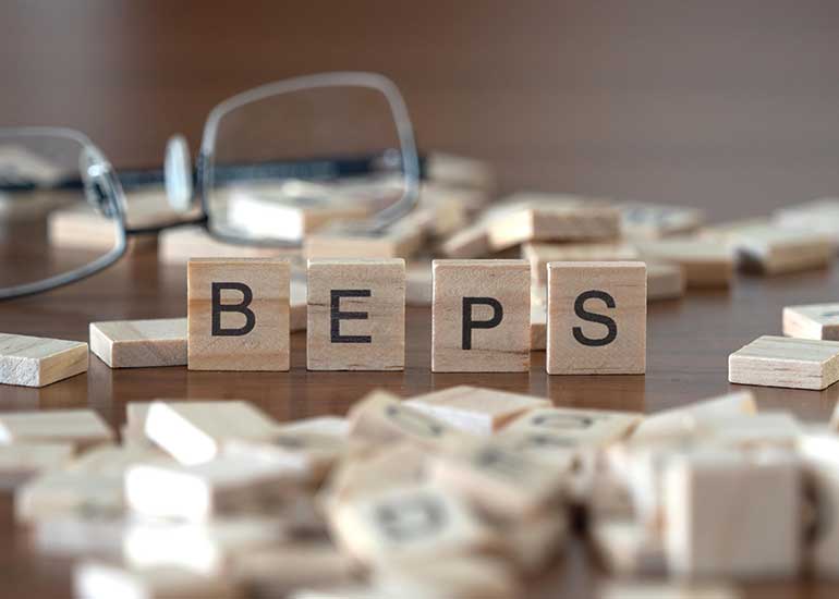 Der Begriff "BEPS" steht für Base Erosion and Profit Shifting. Die Buchstaben "BEPS" stehen jeweils auf einem Holzwürfel auf einem Tisch. Daneben liegen weitere Holzwürfel. Im Hintergrund liegt eine Brille.