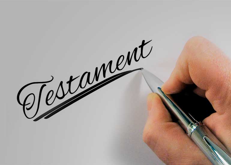 Eine Person schreibt das Wort „Testament” mit einem Kugelschreiber auf ein Blatt Papier.