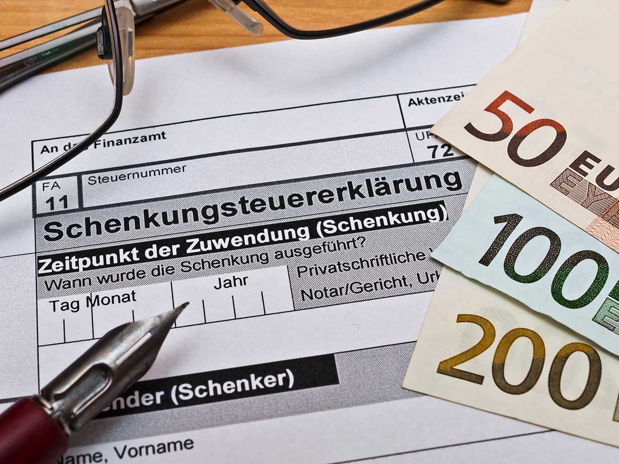 Auf einem Formular zur Schenkungsteuererklärung liegen Euro-Banknoten, ein Stift und eine Brille.