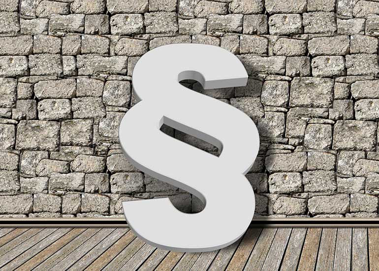 Ein Paragraphenzeichen steht vor einer Steinmauer.