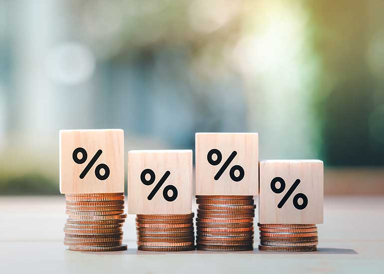 Auf einem Tisch liegen vier Münzstapel. Auf jedem Stapel liegt ein Holzwürfel, auf dem ein Prozentzeichen abgebildet ist.