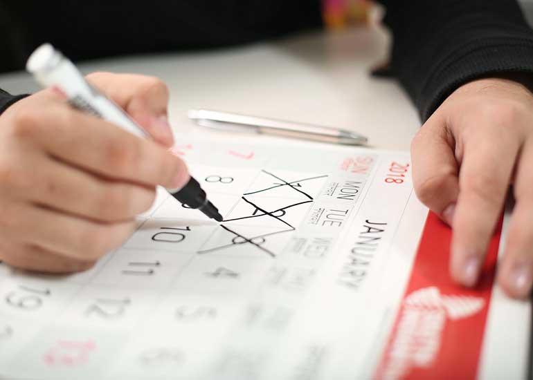 Eine Person sitzt an einem Schreibtisch und durchstreicht Tage auf einem Kalender.