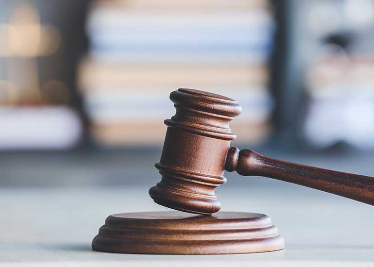 Ein Richterhammer ist auf einem Tisch zu sehen. Im Hintergrund sind Bücherstapel zu erkennen.