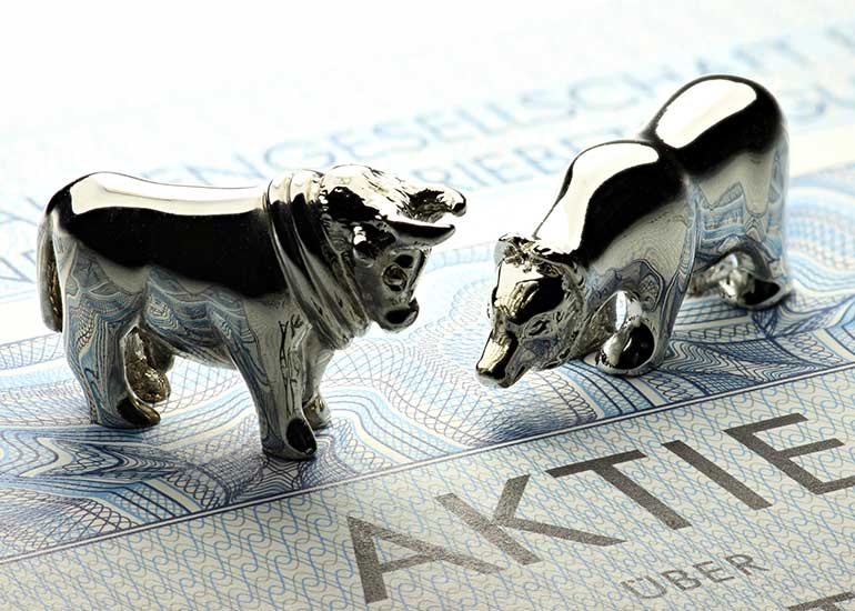 Auf einem Aktienpapier steht eine Modellfigur eines Bullen und eines Bären.