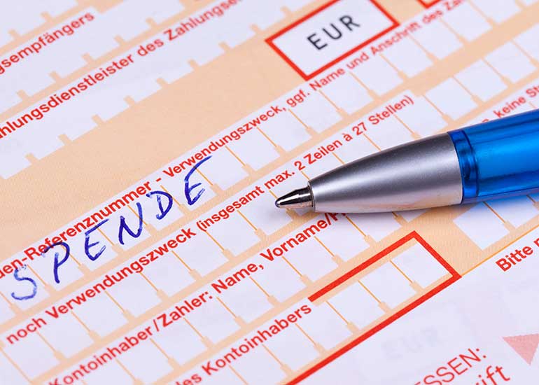 Auf einem Überweisungsformular ist der Begriff „Spende” eingetragen. Auf dem Formular liegt ein Kugelschreiber.