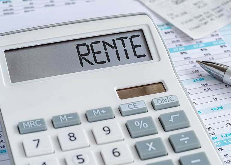 Zu sehen ist ein Taschenrechner, auf dessen Display „Rente” steht. Daneben liegt ein Kugelschreiber und ein Papier mit Zahlentabellen.