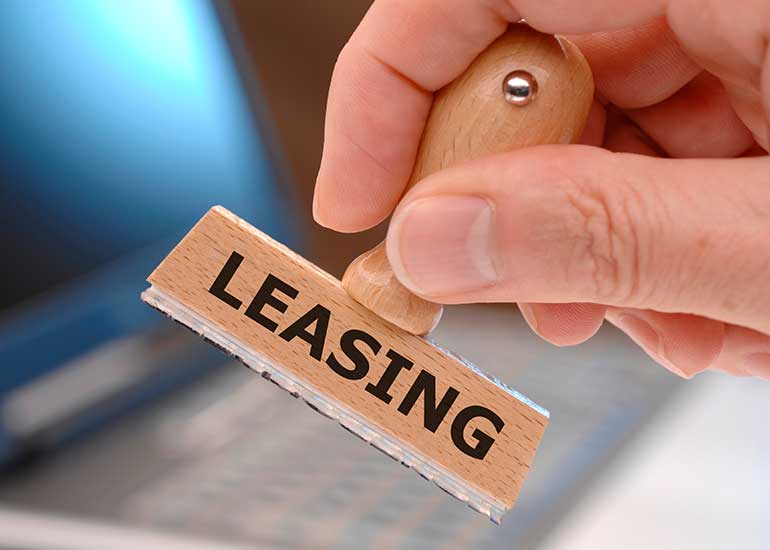 Eine Hand hält einen Stempel mit der Aufschrift „Leasing“. Im Hintergrund ist unscharf ein Laptop zu erkennen.