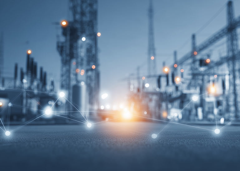 Unscharfe Ansicht eines industriellen Energie- oder Umspannwerks mit technischen Anlagen und Masten. Im Vordergrund sind leuchtende, digital wirkende Verbindungspunkte zu sehen, die ein Netzwerk symbolisieren.