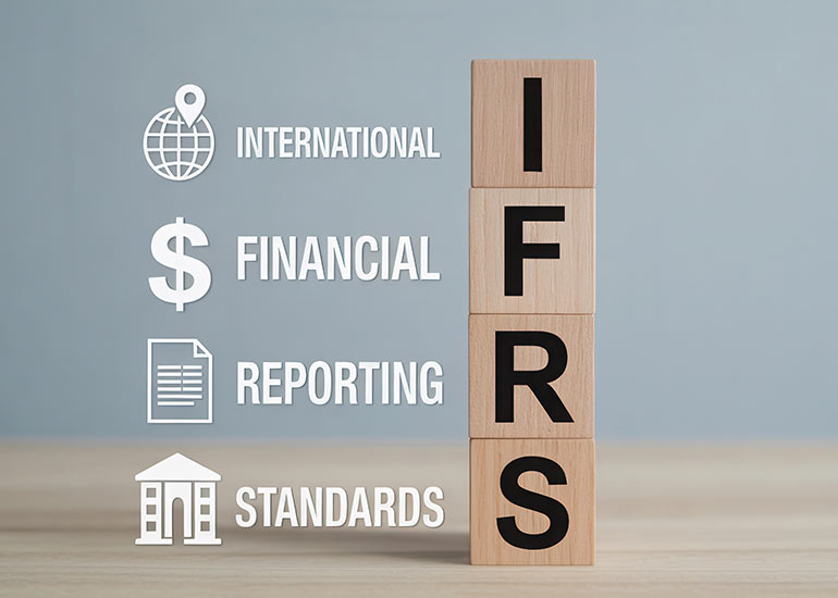 Die Bildcollage zeigt vier Holzklötze, auf denen jeweils ein Buchstabe des Begriffs „IFRS” zu sehen ist. Daneben steht jeweils die Erklärung zur Abkürzung. I steht für International, F für Financial, R für Reporting und S für Standards. Zudem sind den Begriffen Symbole zugeordnet. Dies sind eine Weltkugel für „International”, ein Dollarzeichen für „Financial”, ein Dokument für „Reporting” und ein Haus für „Standards”.