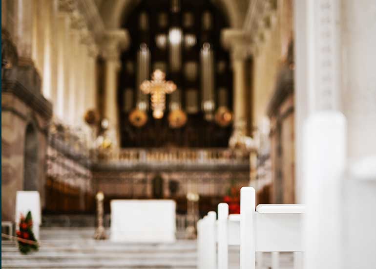 Blick in eine Kirche. Im Vordergrund sind Bänke zu sehen. Im Hintergrund steht ein Altar.