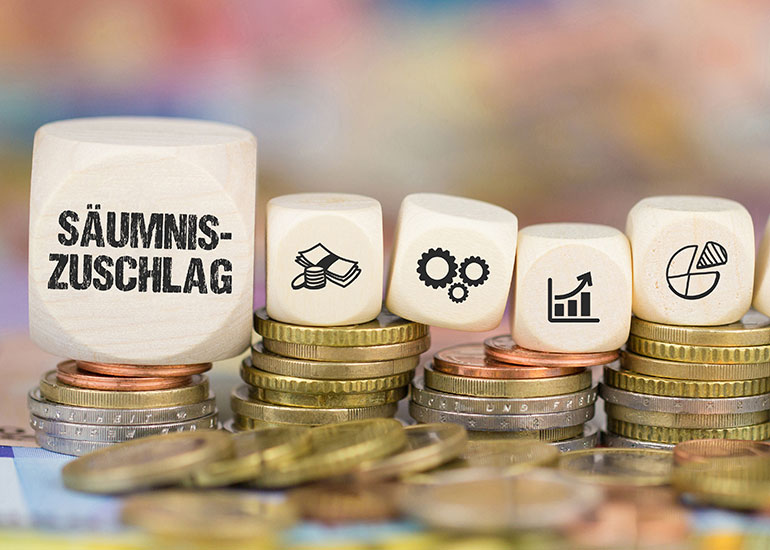 Auf einem Würfel steht „Säumniszuschlag“. Daneben liegen Würfel mit Steuersymbolen. Die Würfel liegen auf Münzstapeln.