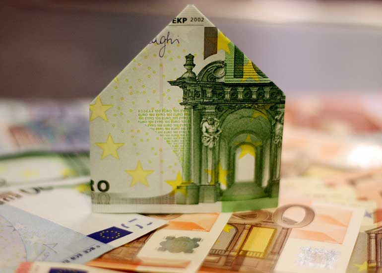 Euro-Banknoten liegen auf einem Tisch. Ein Schein ist zu einem Haus gefaltet und steht über den Scheinen.