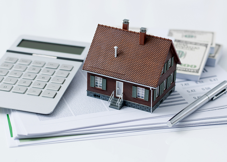 Kleines Hausmodell auf Dokumenten mit Taschenrechner, Stift und Geldscheinen. Die Darstellung steht für Immobilienbewertung, Kaufpreisaufteilung bei bebauten Grundstücken sowie steuerliche und finanzielle Fragestellungen rund um Immobilieninvestitionen.
