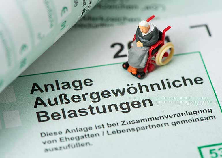 Miniaturfigur in einem Rollstuhl auf einem Steuerformular mit der Überschrift „Anlage Außergewöhnliche Belastungen“.