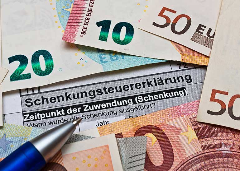 Auf einer Schenkungssteuererklärung liegen Euro-Banknoten und ein Kugelschreiber.