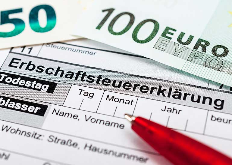 Ein Kugelschreiber liegt auf einer Erbschaftssteuererklärung. Daneben liegen Euro-Banknoten.