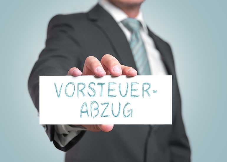 Eine Person im Anzug hält ein Schild mit der Aufschrift „Vorsteuerabzug”.