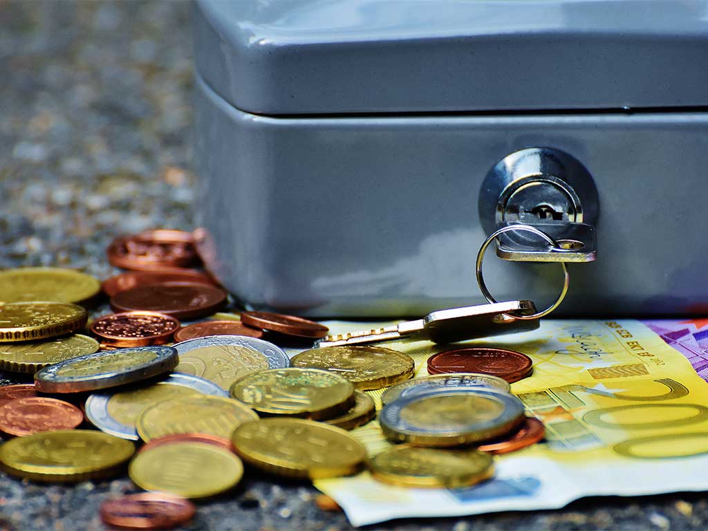Metallene Geldkassette mit eingestecktem Schlüssel, umgeben von Euro-Münzen und Euro-Banknoten.