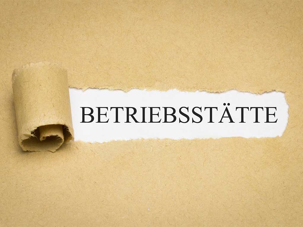 Aufgerissenes Papier mit dem Schriftzug "Betriebsstätte" auf weißem Hintergrund.