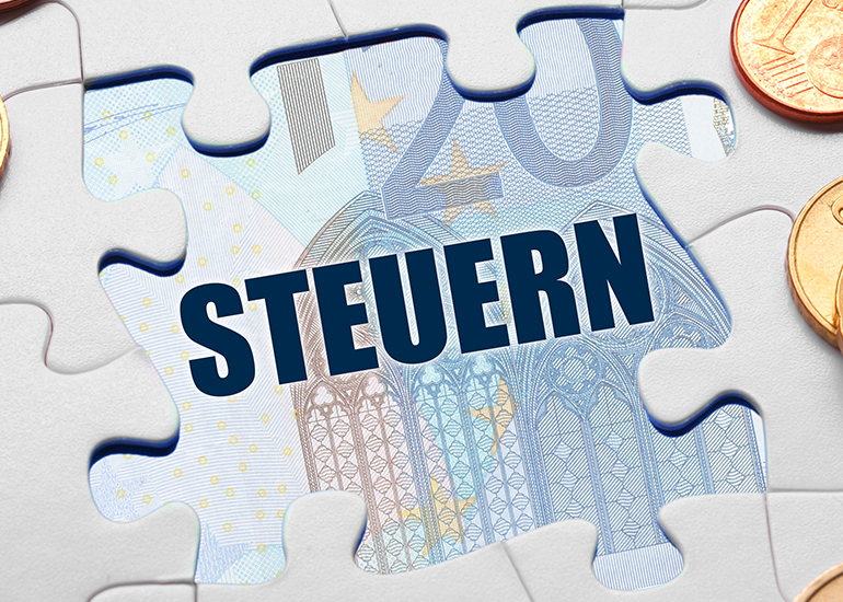 Puzzleteile mit dem Wort ‚"Steuern" geben den Blick auf einen 20-Euro-Schein frei. 