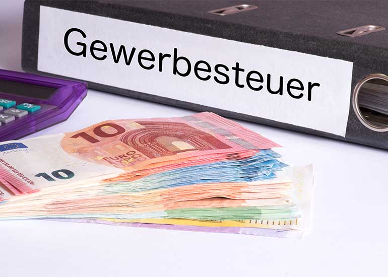 Ein Aktenordner mit der Aufschrift „Gewerbesteuer” liegt neben Euro-Banknoten und einem Taschenrechner.