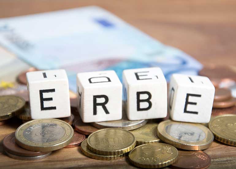 Weiße Buchstabenwürfel mit dem Wort „Erbe“ liegen auf Euro-Münzen und Geldscheinen.