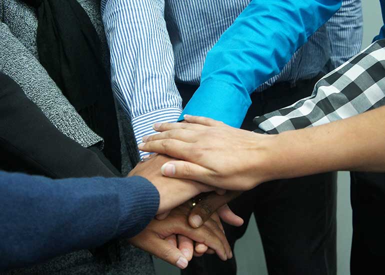 Mehrere Personen legen ihre Hände übereinander und bilden ein Teamzeichen.